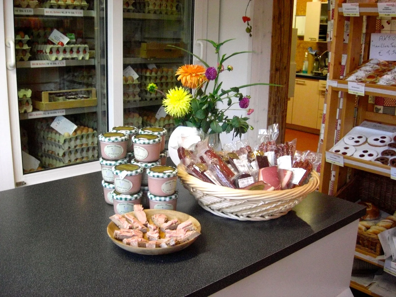 Theke im Sennhof Lädele mit dem Kühlschrank voller Eier, Honiggläsern, einem Korb mit Kaminwurzen und einem Blumenstrauß