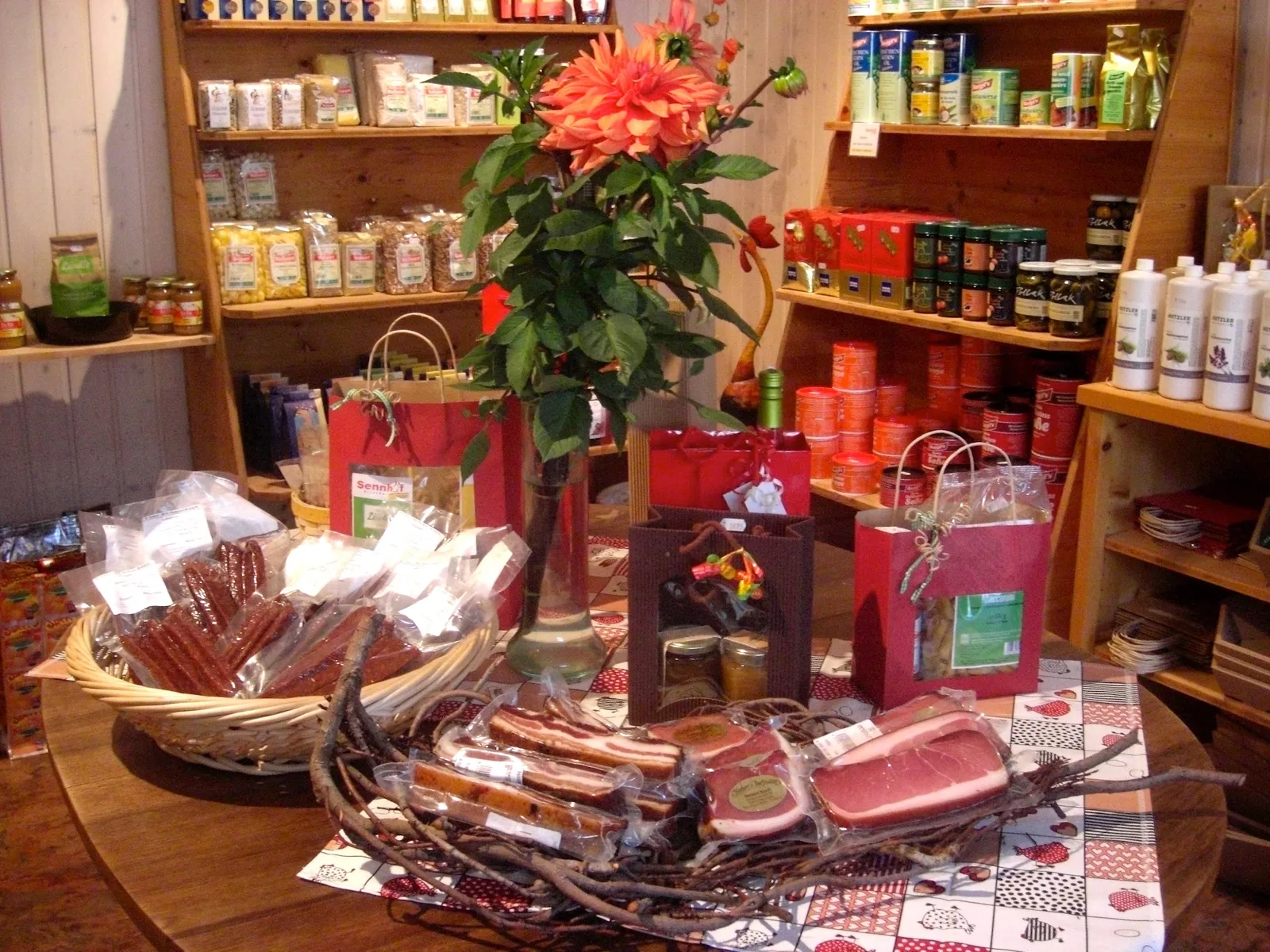 Blick in den Laden: Holzregale mit Eingemachtem, Geschenktaschen und ein Korb mit Kaminwurzen und Speck auf dem Tisch